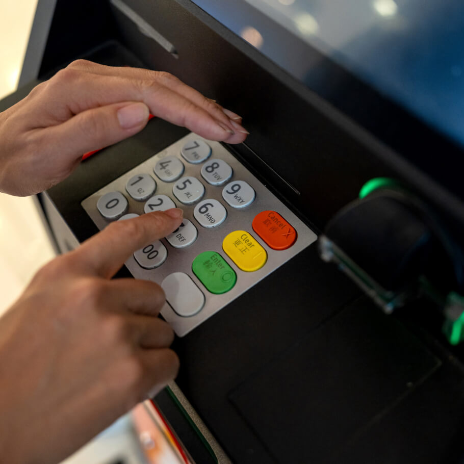 Donna che digita il PIN all'ATM comprendo la tastiera con la mano.